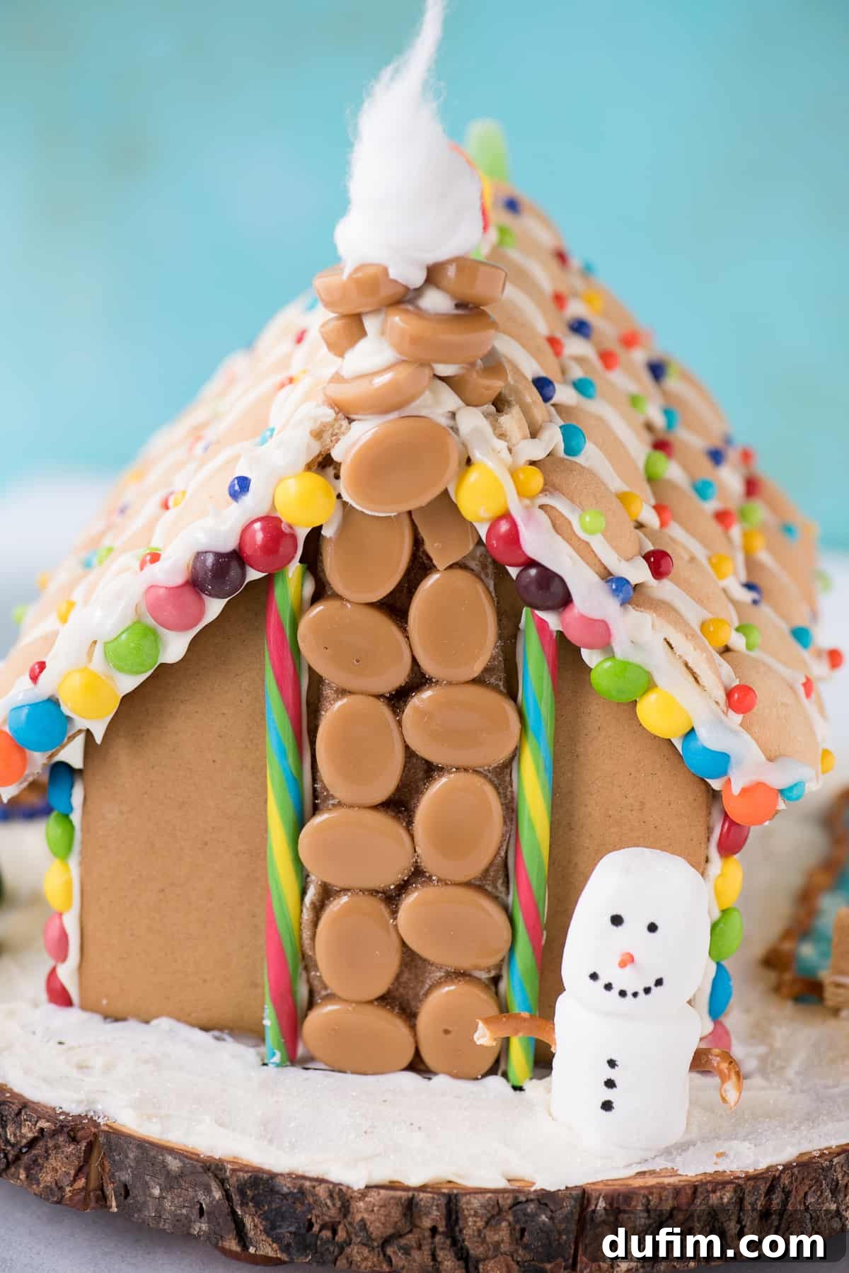 A child's hand reaches for a gingerbread house, symbolizing the joy and interaction of decorating.