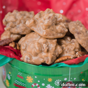 A festive green tin filled with rich pecan pralines sits on red and green tissue paper. The golden-brown, chunky pecan pralines are glossy and surrounded by whole pecans, with holiday decorations printed on the tin.