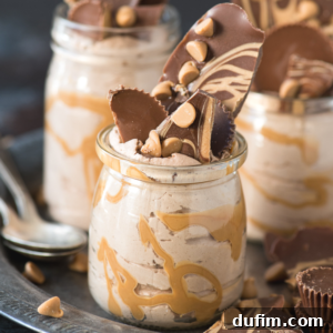 A small jar filled with creamy chocolate peanut butter mousse, swirled with peanut butter, topped with chocolate shards and peanut butter chips. Spoons and more mousse jars are in the background.