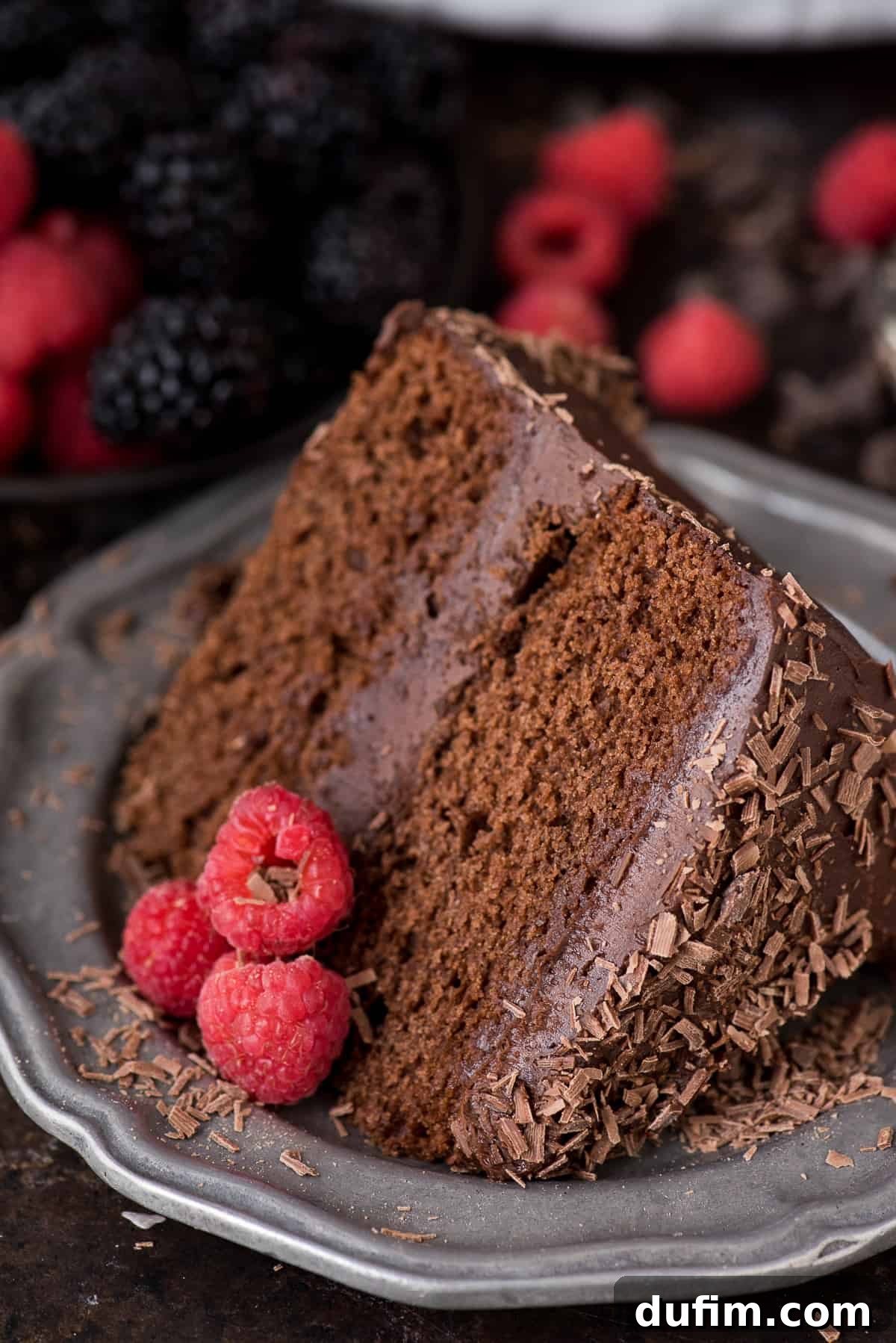 A close-up of a slice of chocolate velvet cake, showcasing the moist layers and rich chocolate buttercream, garnished with fresh raspberries and blackberries.