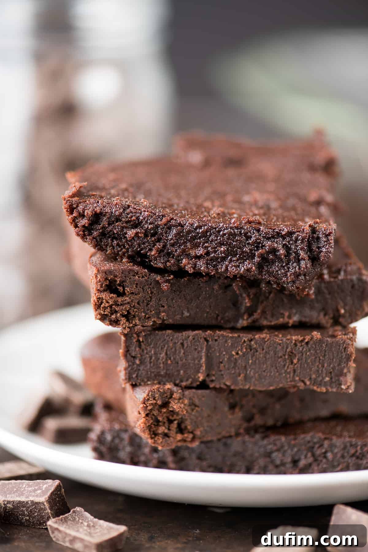 Five healthier fudgy brownies surrounded by chocolate on a white plate, showcasing their rich texture.