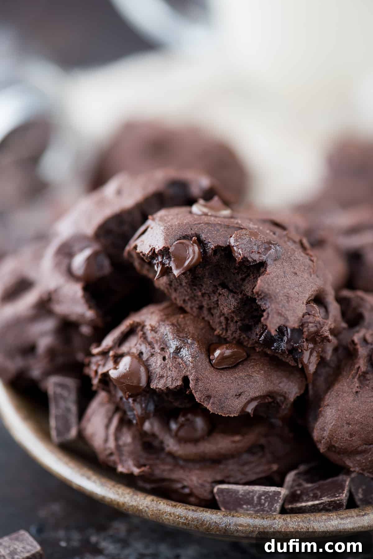 Enjoying a Healthier Dark Chocolate Coconut Oil Cookie A healthier dark chocolate coconut oil cookie with a bite taken out, resting on a stack of other cookies on a decorative plate.
