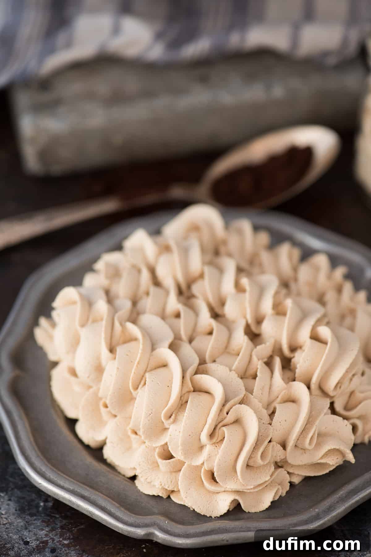 Beautifully piped swirls of creamy coffee whipped cream are elegantly presented on a sleek metal plate against a dark, dramatic background.