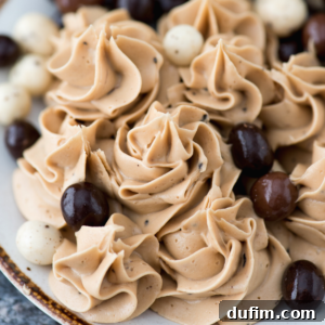 Swirls of light brown coffee mousse with a hint of coffee frosting, topped with scattered dark and white chocolate-covered espresso beans on a plate.