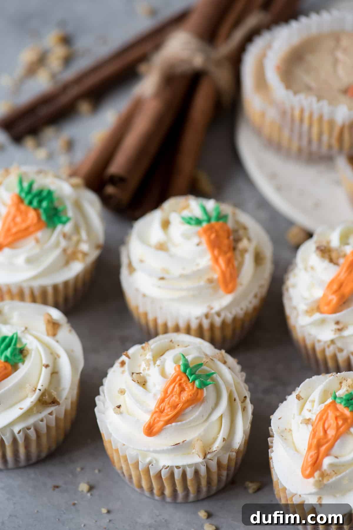 Spiced Carrot Cheesecake Minis 2 Mini Carrot Cheesecakes made in a muffin pan, adorned with light frosting and miniature carrot decorations.