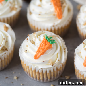 Cupcakes topped with swirls of white frosting, sprinkled with chopped nuts, and decorated with small orange carrot-shaped icing decorations—perfect for fans of mini carrot cake cheesecakes.