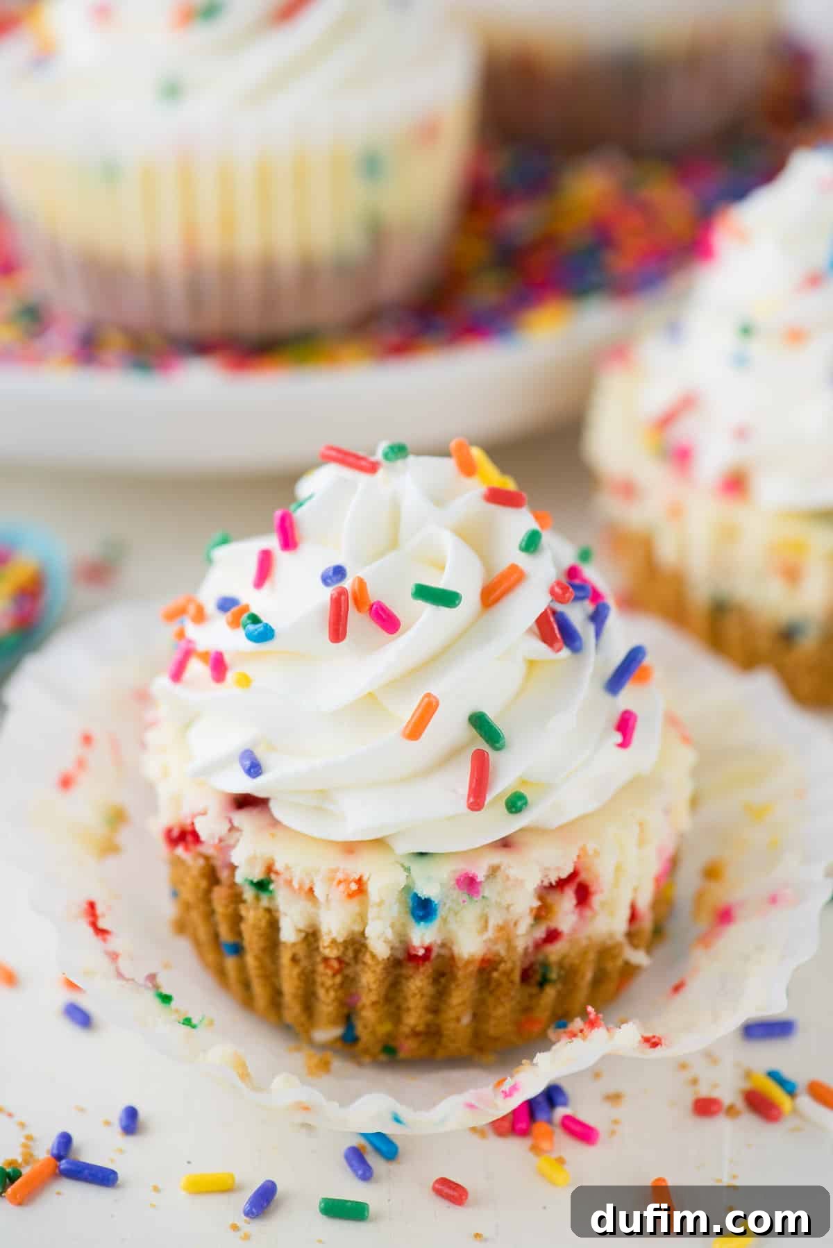 A duo of mini funfetti cheesecakes, beautifully topped with vibrant rainbow sprinkles, ready to be served on a pristine white surface.
