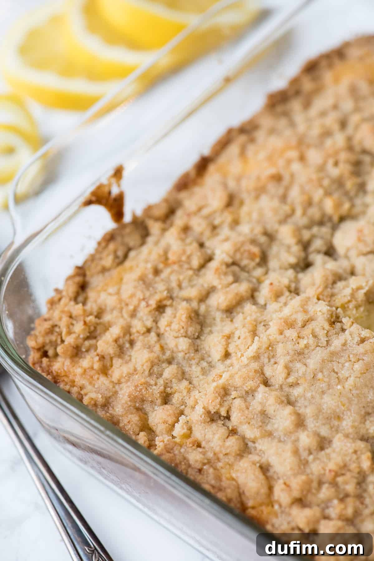 The soft, yellow interior of the lemon crumb cake is visible, topped with a generous layer of golden, buttery crumbs.