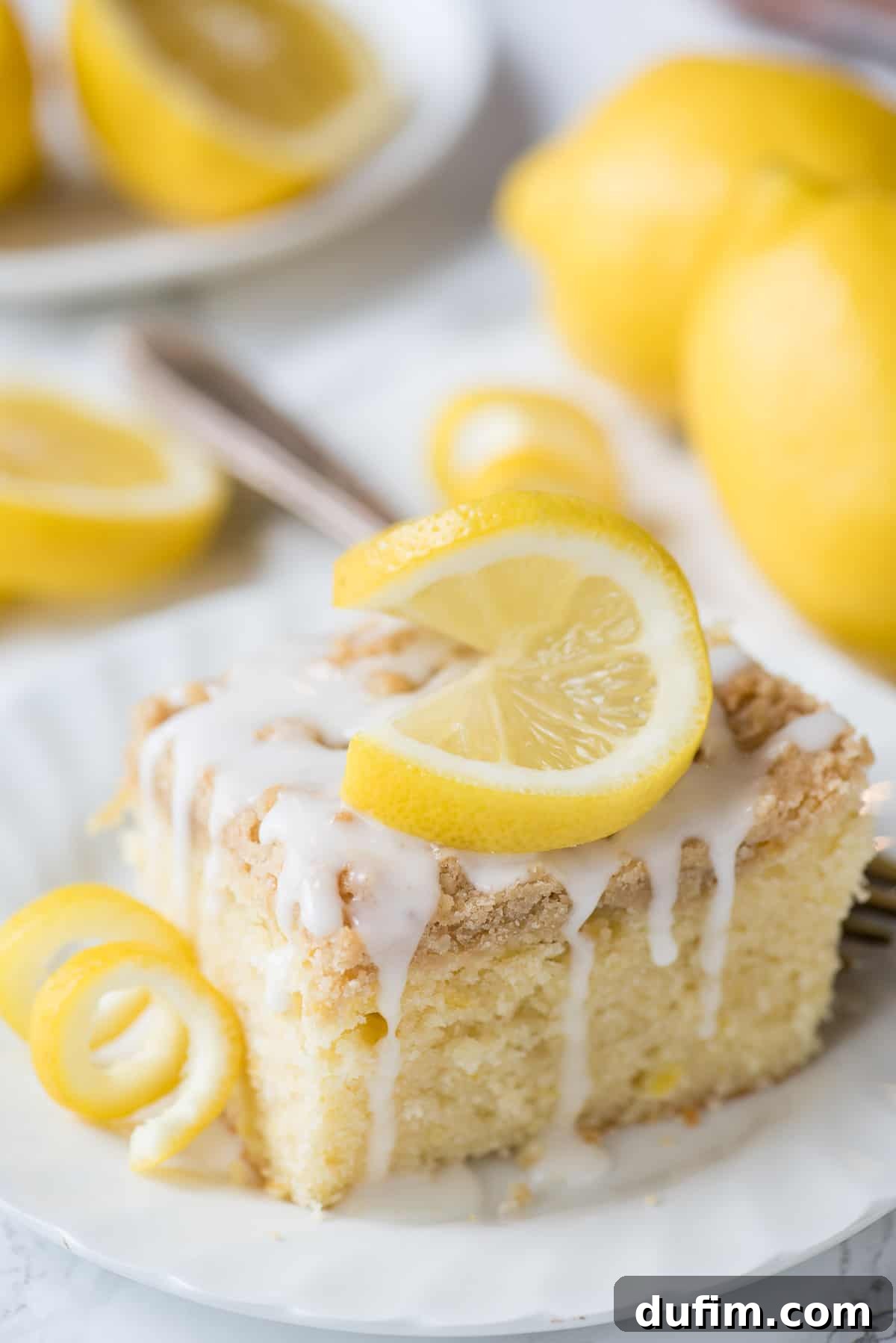 Four generous slices of lemon crumb cake are arranged on a white serving dish, each showcasing the golden crumb topping.