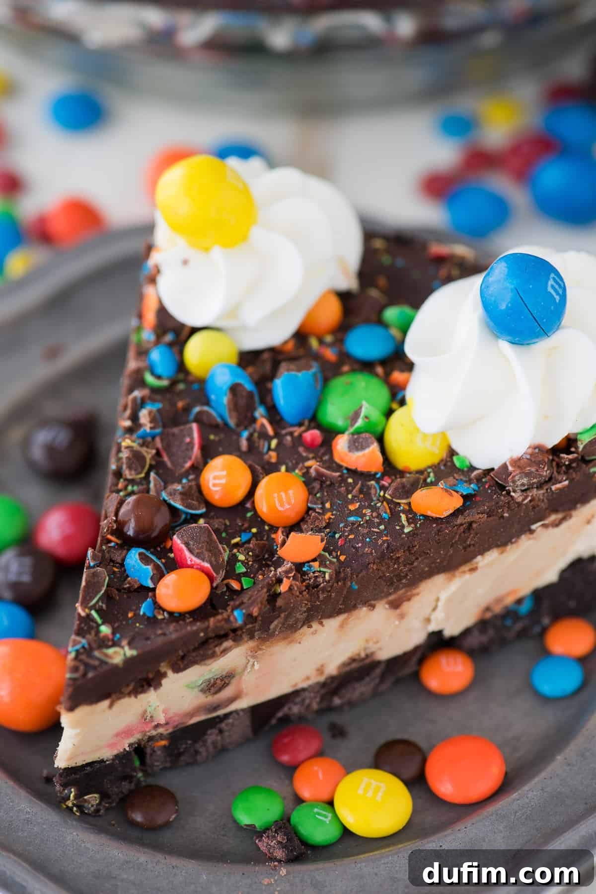 M&M No-Bake Dream Pie 5 An overhead shot of the completed No-Bake M&M Pie, elegantly decorated with swirls of whipped cream and a generous scattering of vibrant M&M candies, sitting perfectly on a pie stand, ready to be enjoyed.