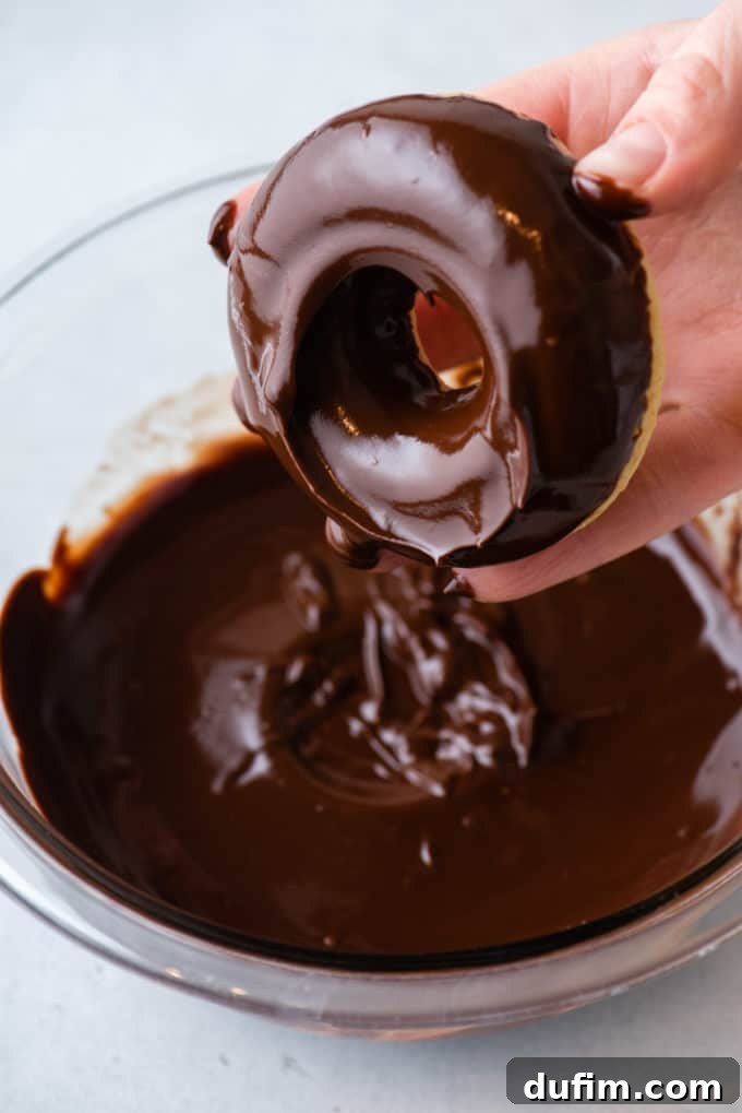 A baked donut being dipped into a luscious chocolate glaze, creating an inviting swirl of sweetness.