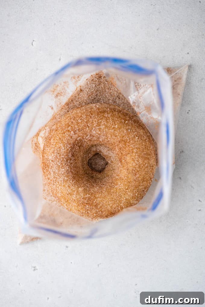 A freshly baked donut nestled in a Ziploc bag, being shaken to coat it thoroughly with cinnamon sugar.