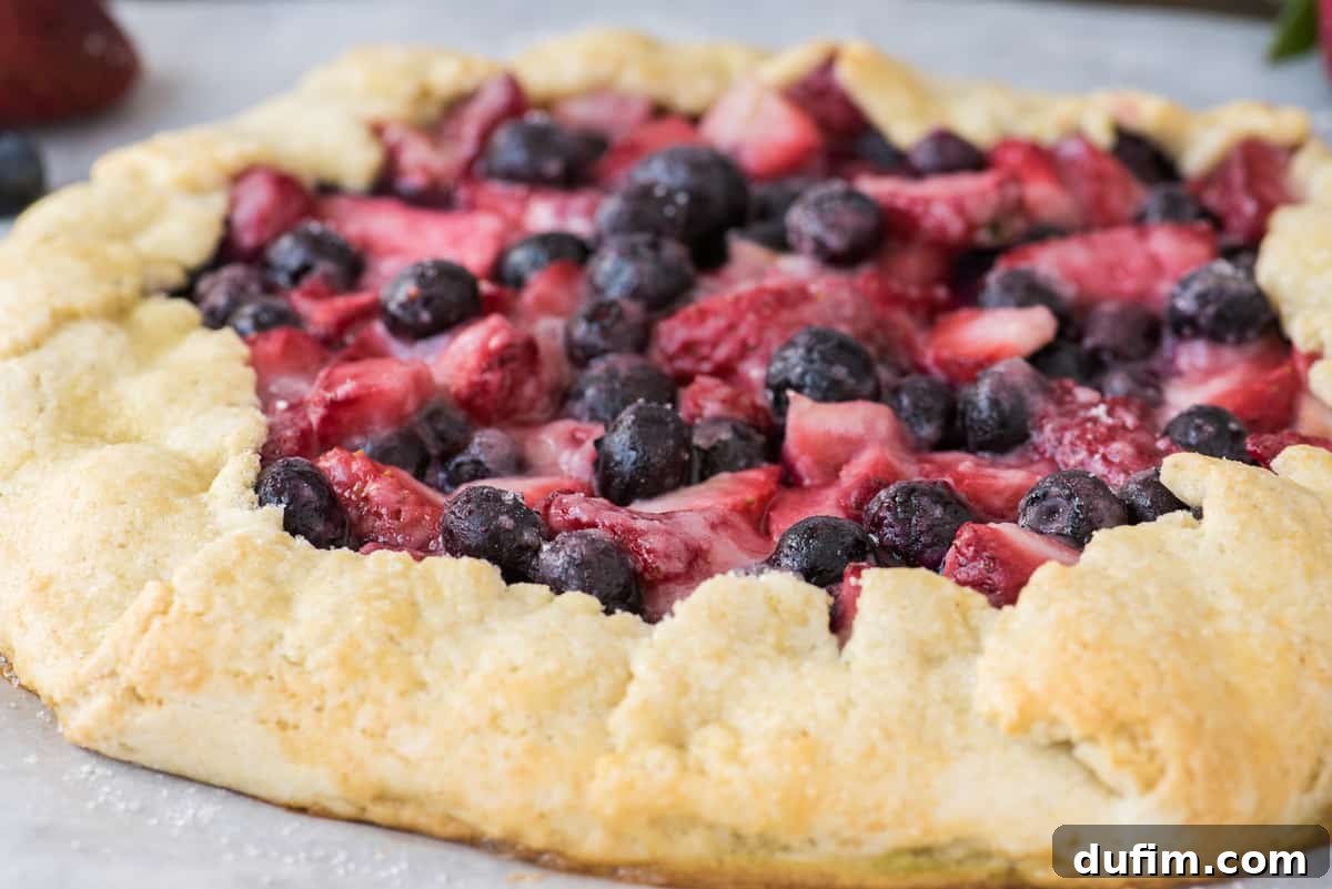 Close-up of a freshly baked mixed berry galette, showcasing the vibrant colors of strawberries, blueberries, and blackberries peeking from under a perfectly golden, crimped pastry crust.