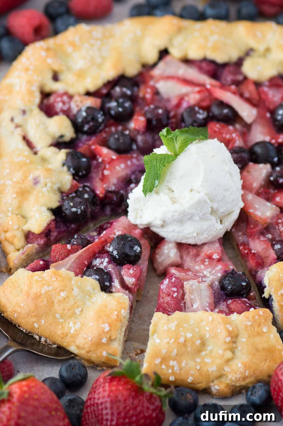 Warm mixed berry galette on a metal baking sheet, topped with a generous scoop of vanilla ice cream, ready to be enjoyed.