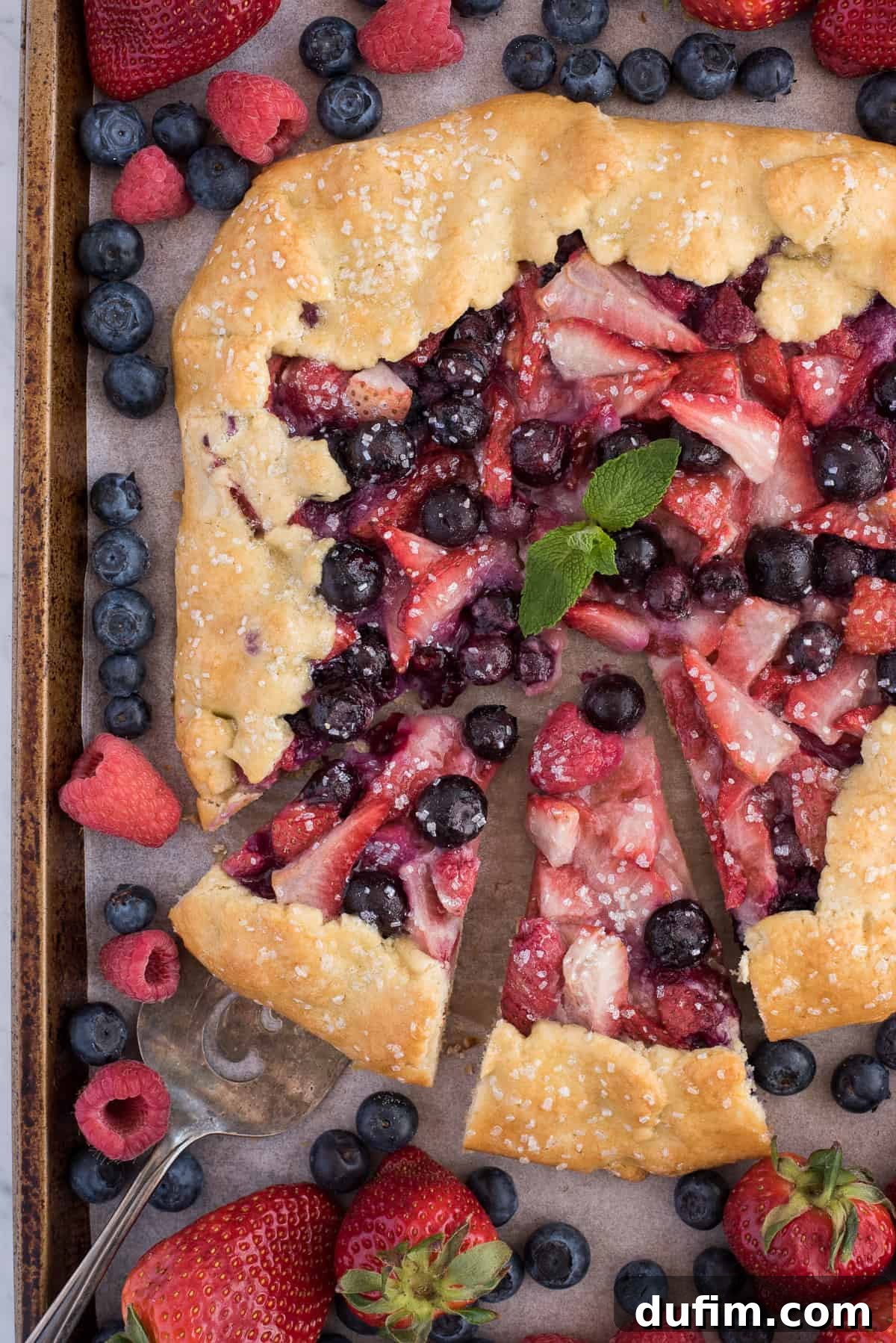 Freshly baked mixed berry galette adorned with mint leaves on a metal baking sheet, ready to be sliced and served.