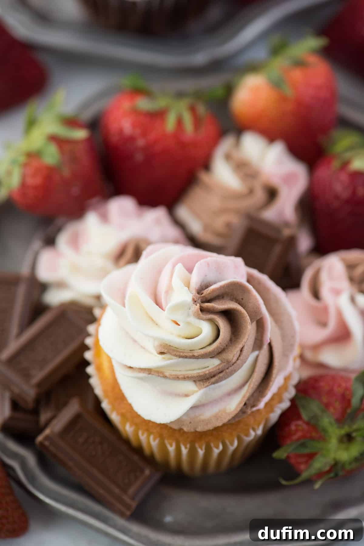 A charming cupcake topped with perfectly swirled Neapolitan whipped cream, showcasing the distinct vanilla, chocolate, and strawberry layers.