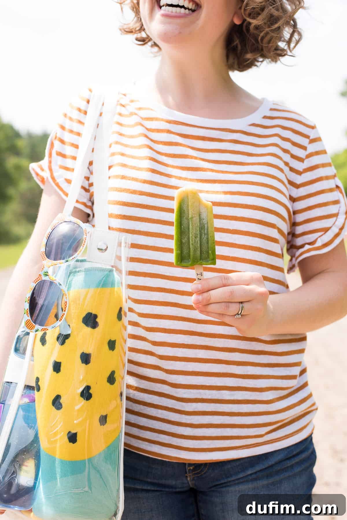 Close-up view of two-layered green and yellow popsicles, featuring spinach and mango, nestled in a gray bowl on a pristine white background.