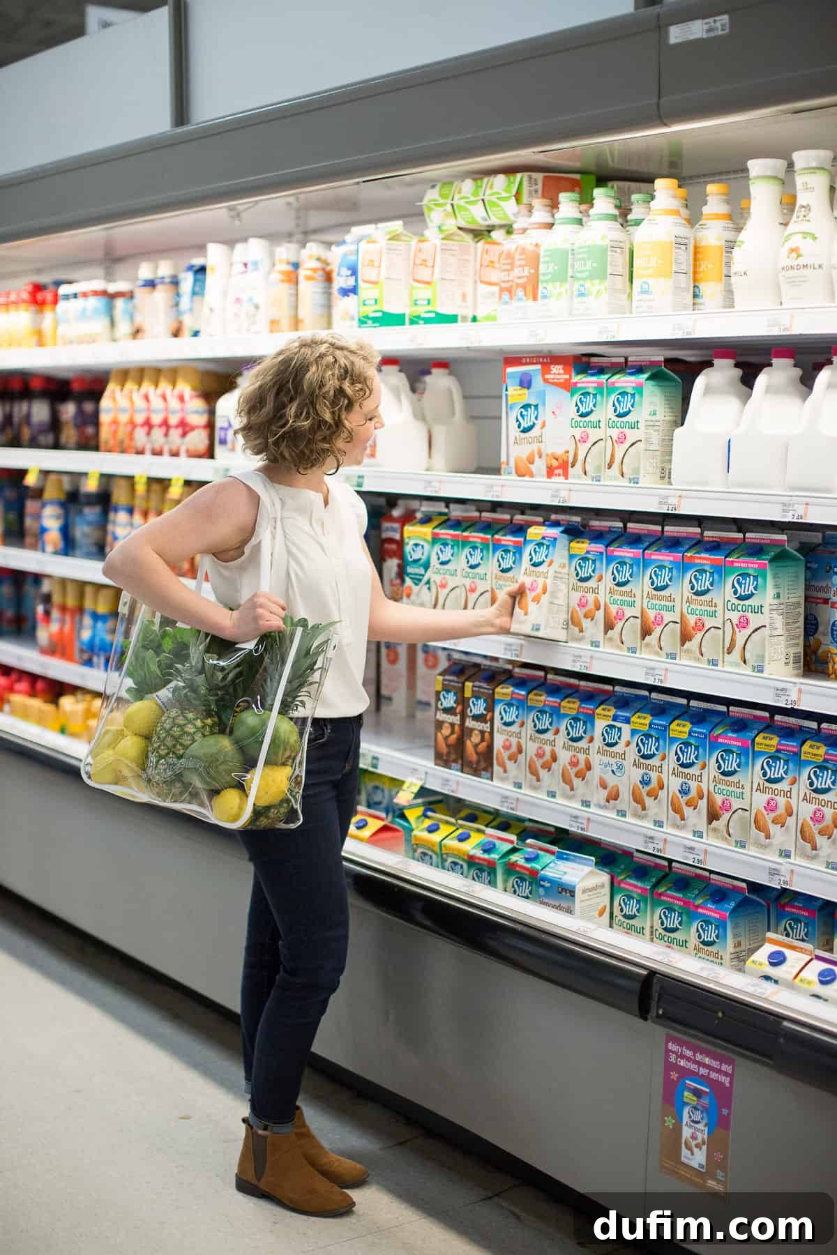 A woman in a grocery store aisle, reaching for a carton of almond milk, capturing an authentic moment of healthy grocery shopping.