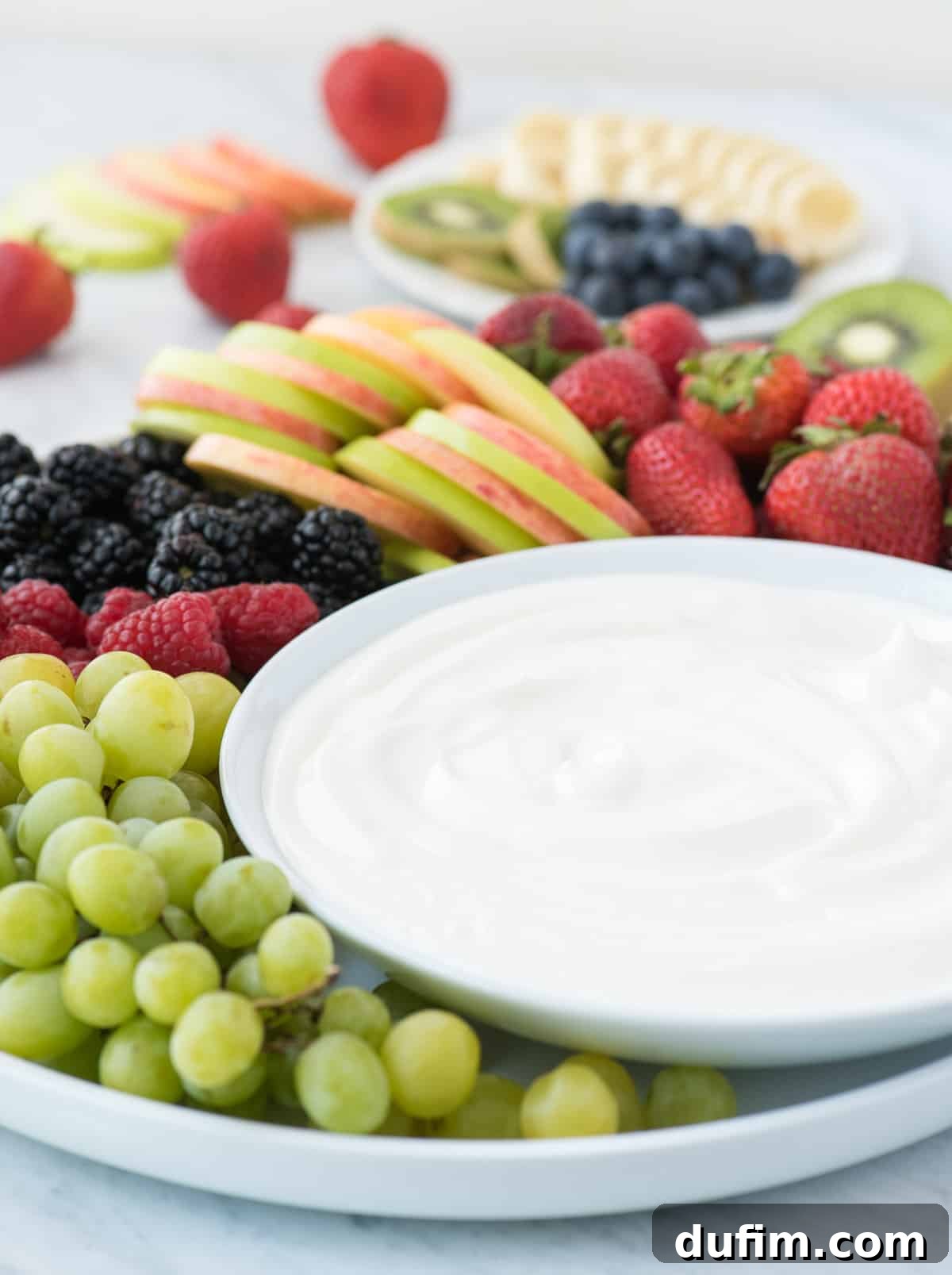 The ultimate 3-ingredient fruit dip with marshmallow fluff – a dreamy, no cream cheese treat! A close-up shot of the white fruit dip nestled in a bowl, surrounded by a colorful array of fresh fruits like strawberries, grapes, and apple slices, inviting guests to dip and enjoy.