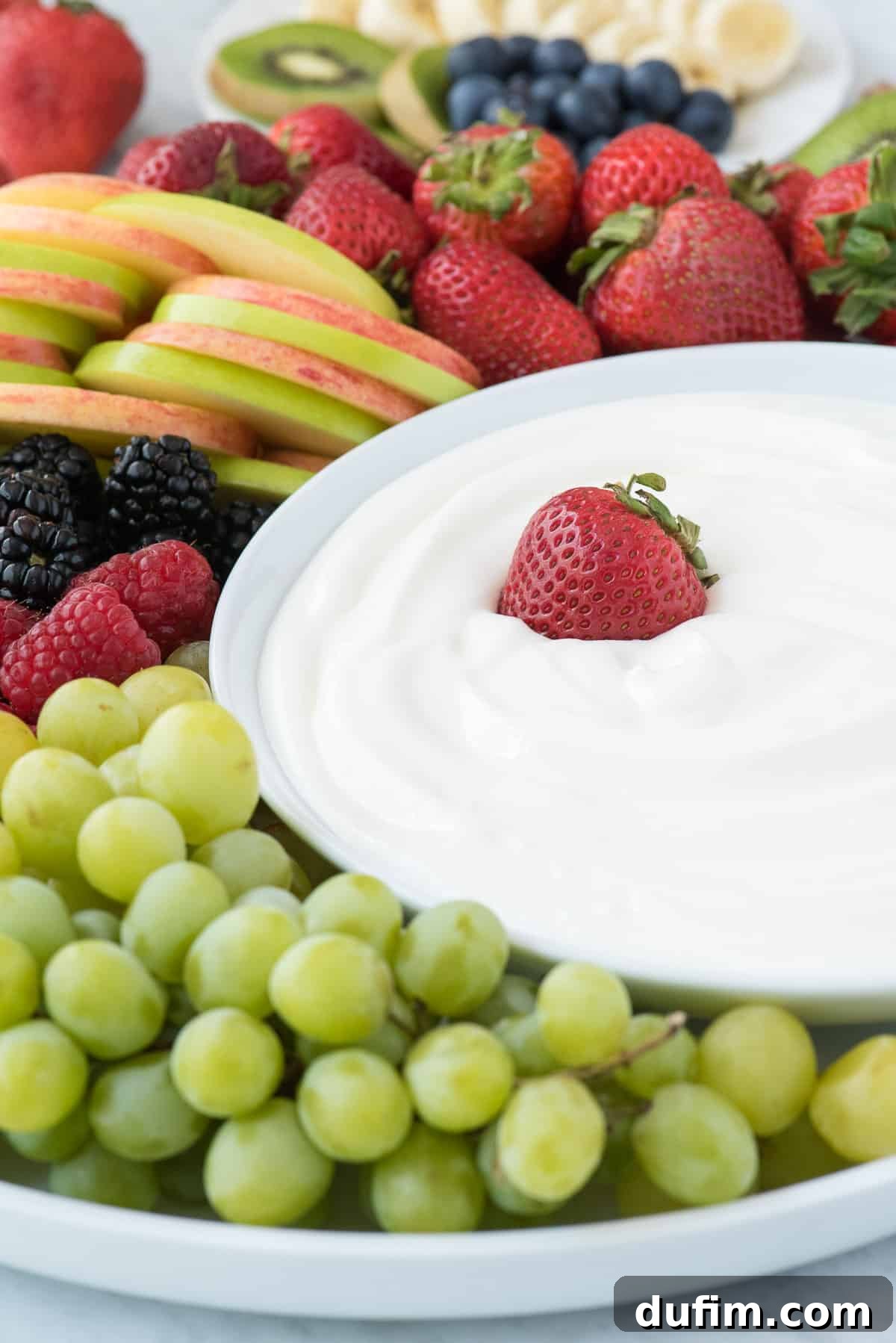 Serve this easy 3-ingredient marshmallow fruit dip with your favorite fresh fruits! A tantalizing spread of fresh, colorful fruits including bright strawberries, crisp green apples, dark berries, and grapes, arranged around a central bowl of smooth, white marshmallow fruit dip, ready for sharing.