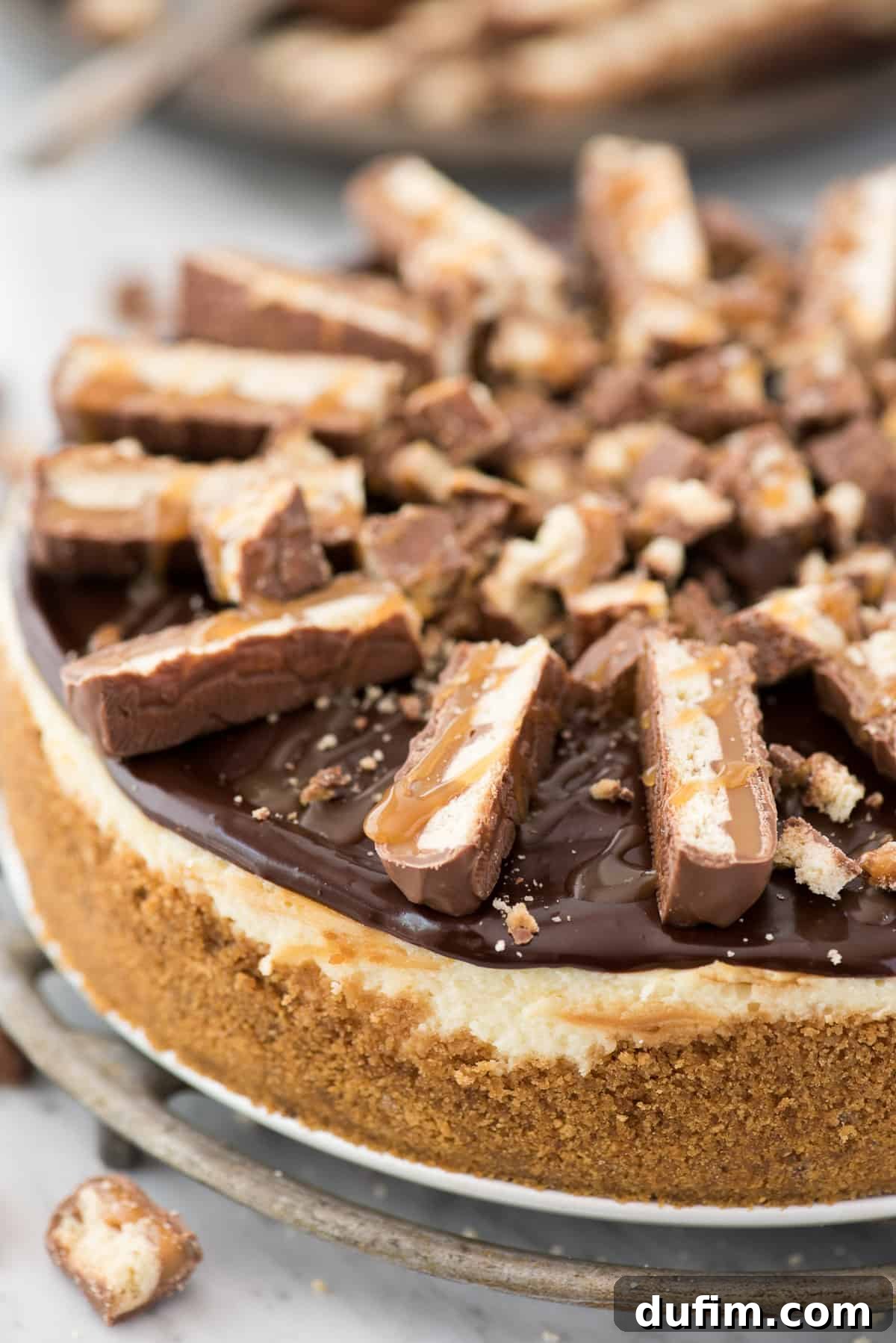Experience all your favorite Twix flavors in this irresistible cheesecake: crunchy crust, rich caramel, and decadent chocolate, crowned with Twix candy. A close-up of a finished Twix cheesecake slice, showing the distinct layers of graham cracker crust, creamy caramel cheesecake, and chocolate ganache, garnished with Twix chunks.
