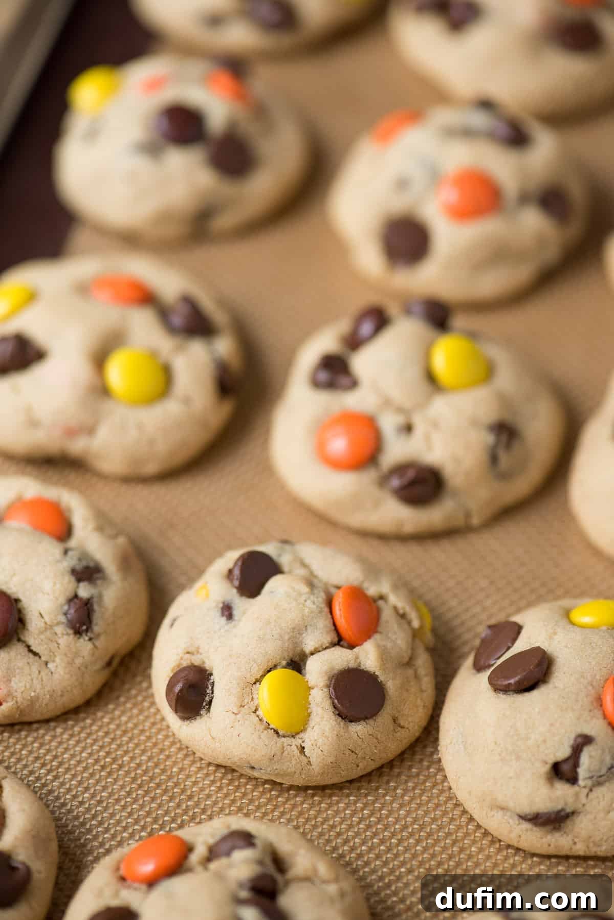 More peanut butter cookies with Reese's Pieces candies and chocolate chips on a metal baking sheet