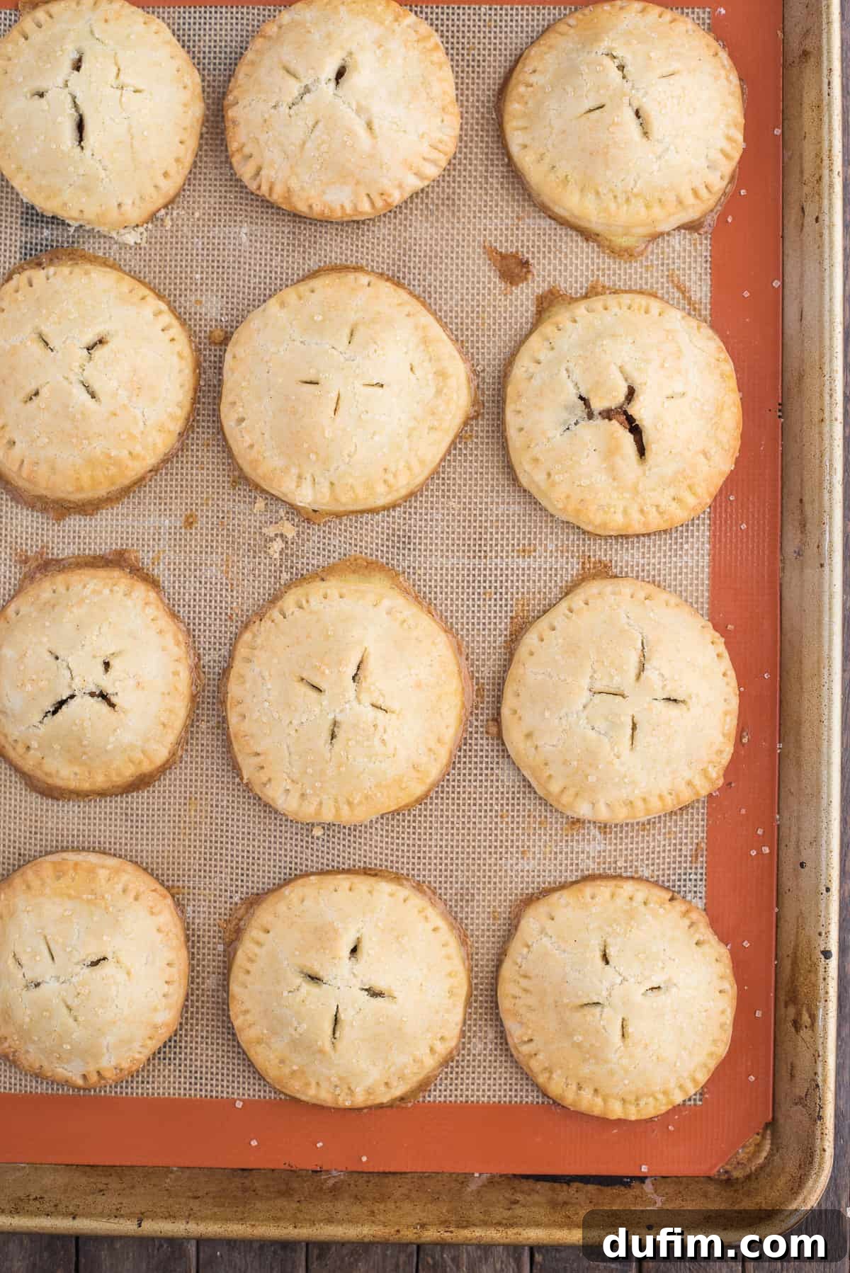 Homemade apple hand pies are a great apple dessert to make any time of the year. Watch the quick step by step video to learn how to make these mini apple pies. #applehandpies #handpies #applepie #minipie A baking sheet lined with silicone mat, holding several unbaked apple hand pies that are perfectly crimped and ready for the oven, illustrating the chilling step before baking.