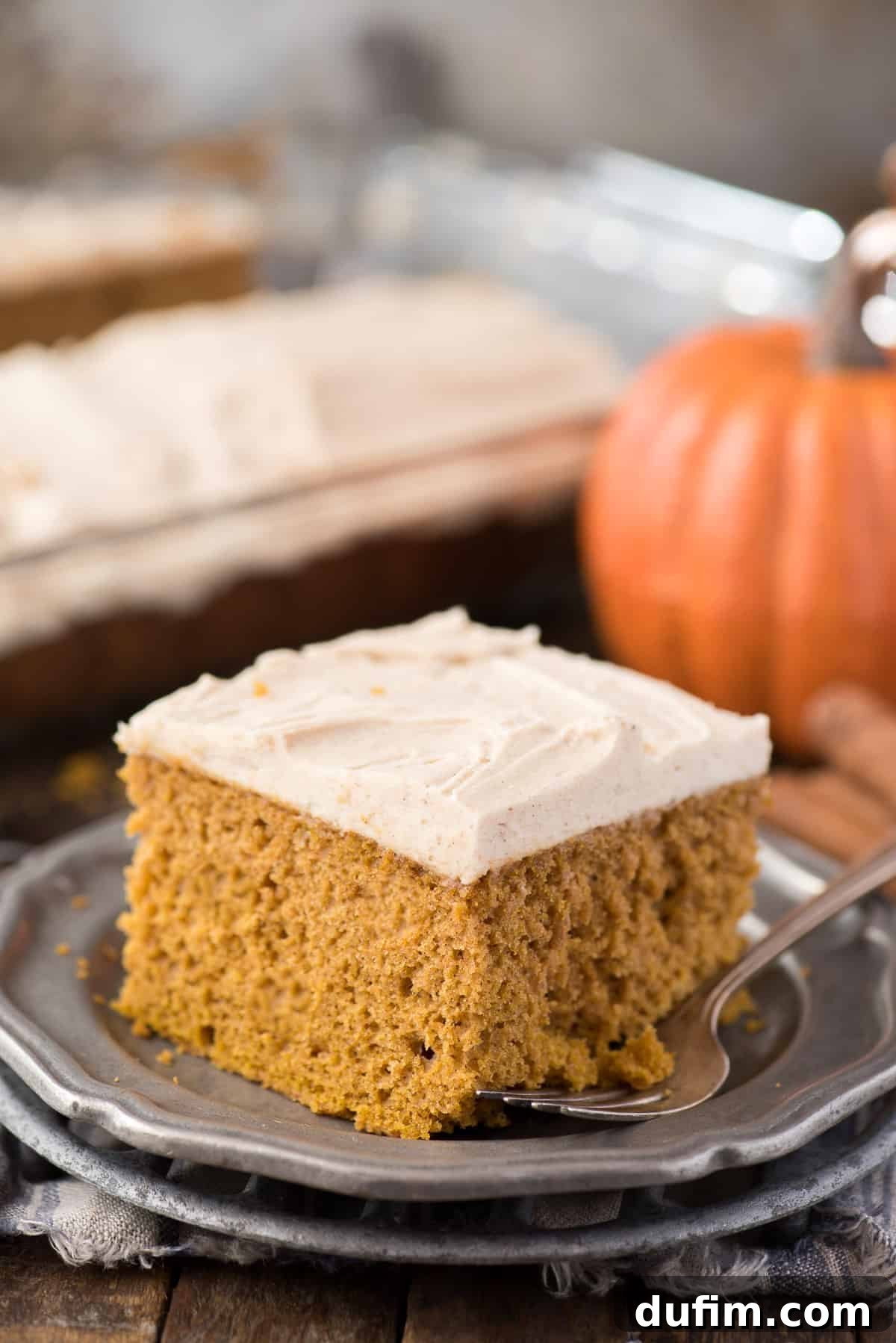 Effortless Pumpkin Cake from a Mix 2 A beautifully moist slice of pumpkin cake on a metal plate with fresh pumpkins in the background, hinting at autumn flavors.