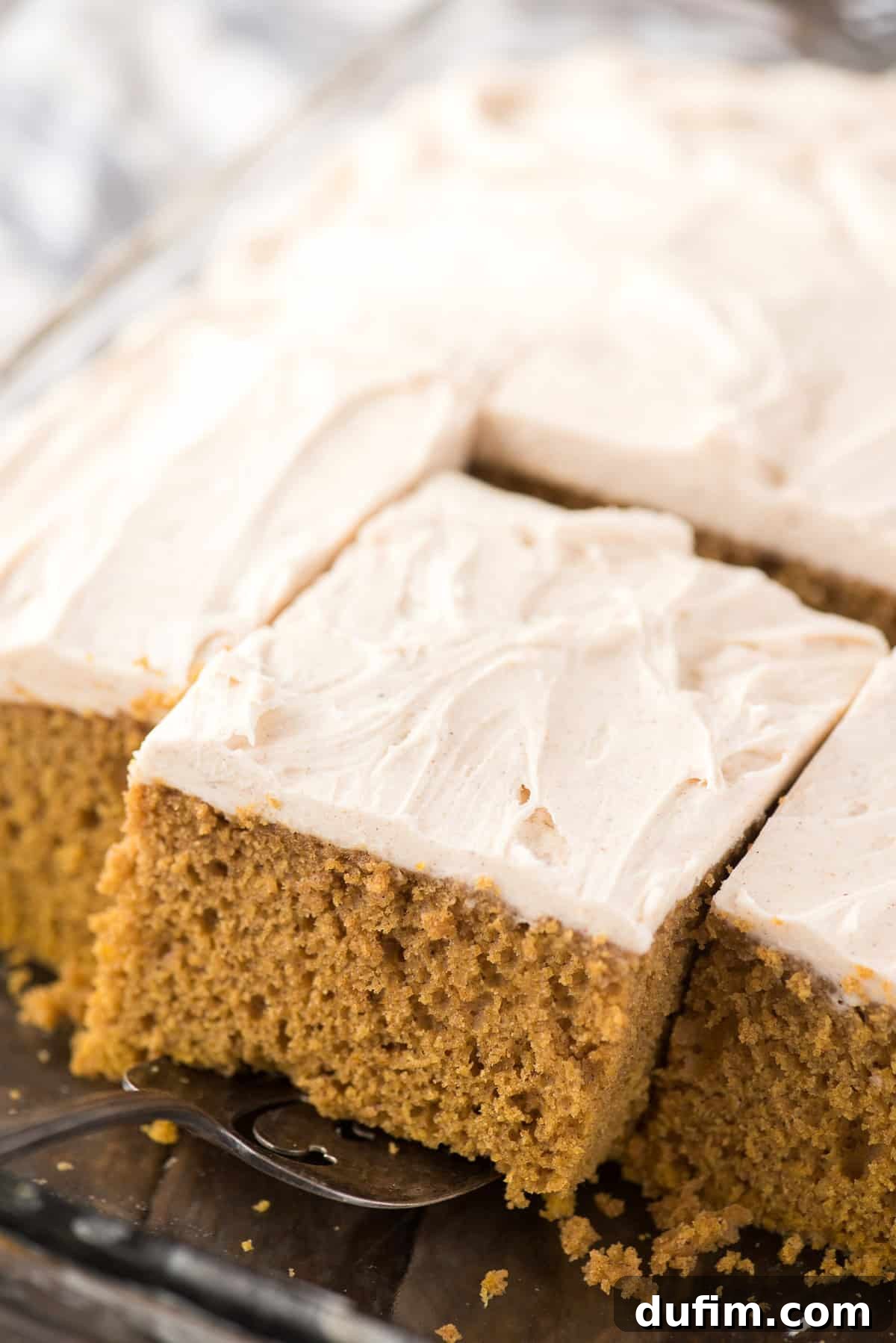 Effortless Pumpkin Cake from a Mix 3 A perfect slice of pumpkin cake being lifted from a clear glass 9x13 inch baking pan with a metal spatula, showcasing its moist texture.