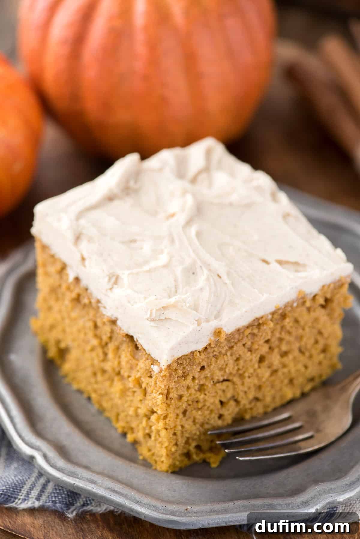 Effortless Pumpkin Cake from a Mix 5 A generous slice of moist pumpkin cake, topped with creamy frosting, served on a metal plate. A hint of autumn decor is visible in the background.