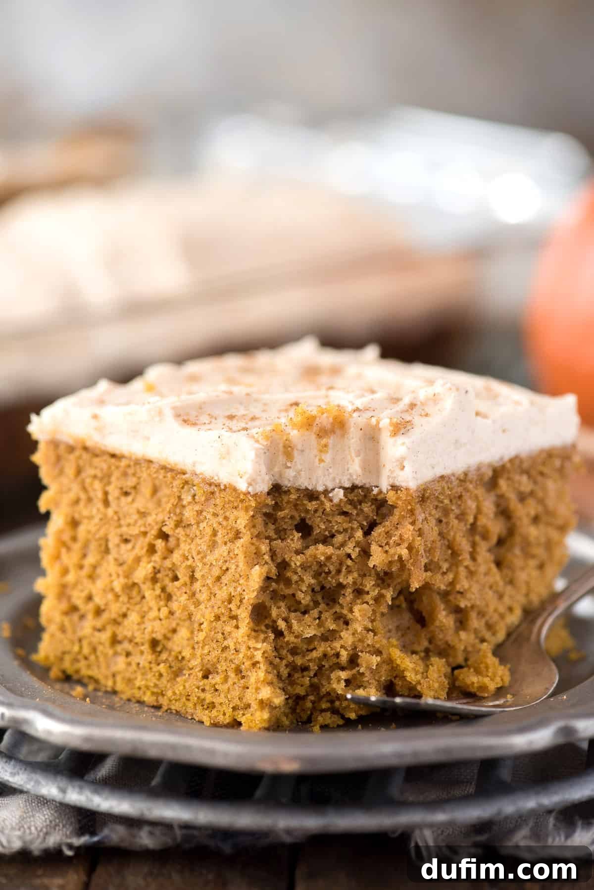 Effortless Pumpkin Cake from a Mix 6 Another enticing slice of moist pumpkin cake on a metal plate, with decorative pumpkins in the background, ready to be enjoyed.