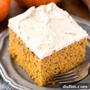A square slice of moist, easy pumpkin cake with creamy white frosting sits on a gray plate, with a fork beside it.