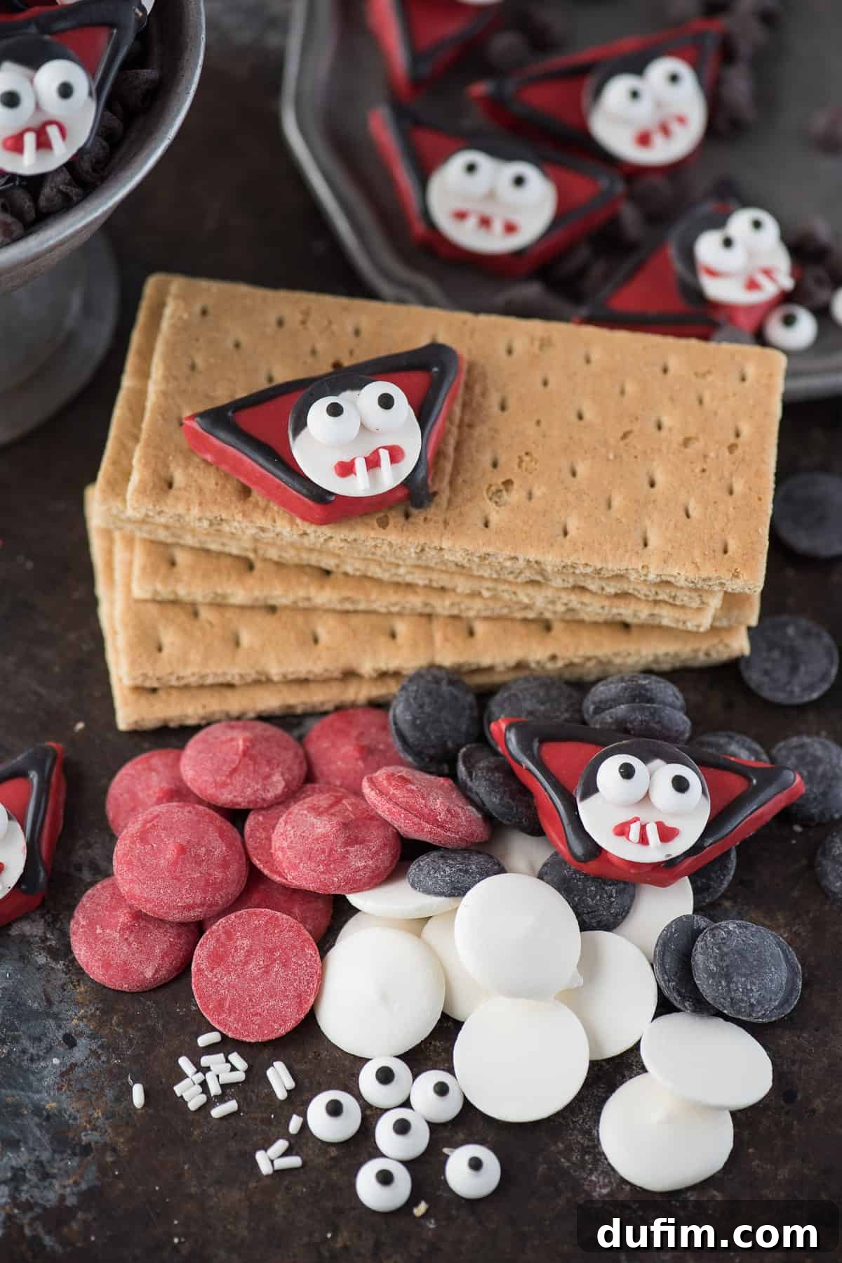 Essential supplies laid out for crafting edible vampire treats, including crisp graham crackers, vibrant red, black, and white candy melts, and playful candy eyeballs – perfect for your next Halloween creation.