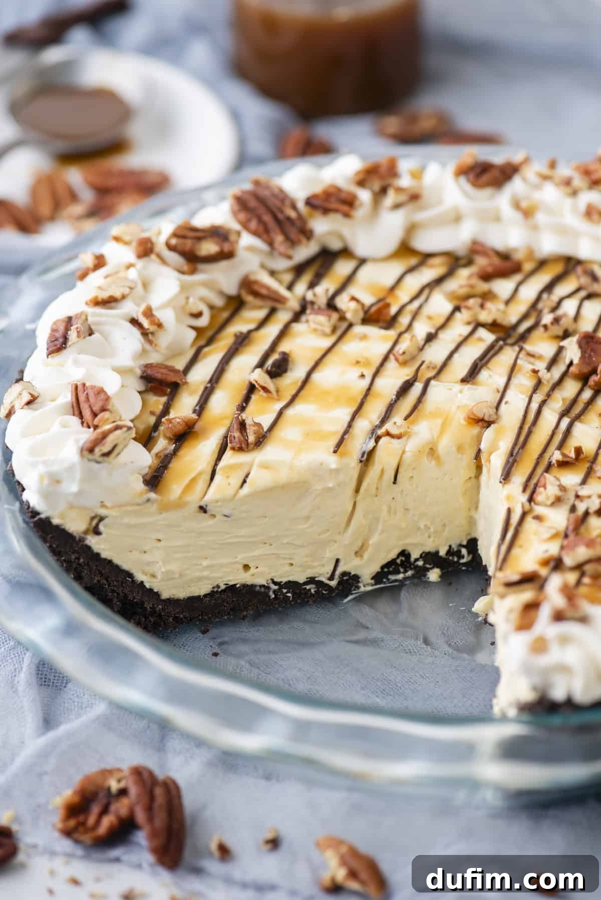 Caramel Pecan Chocolate Indulgence 2 A stunning no-bake Turtle Pie in a clear glass pie dish, generously topped with golden caramel, rich chocolate drizzles, fluffy whipped cream, and crunchy pecans, with extra pecan pieces scattered artfully around the dish.