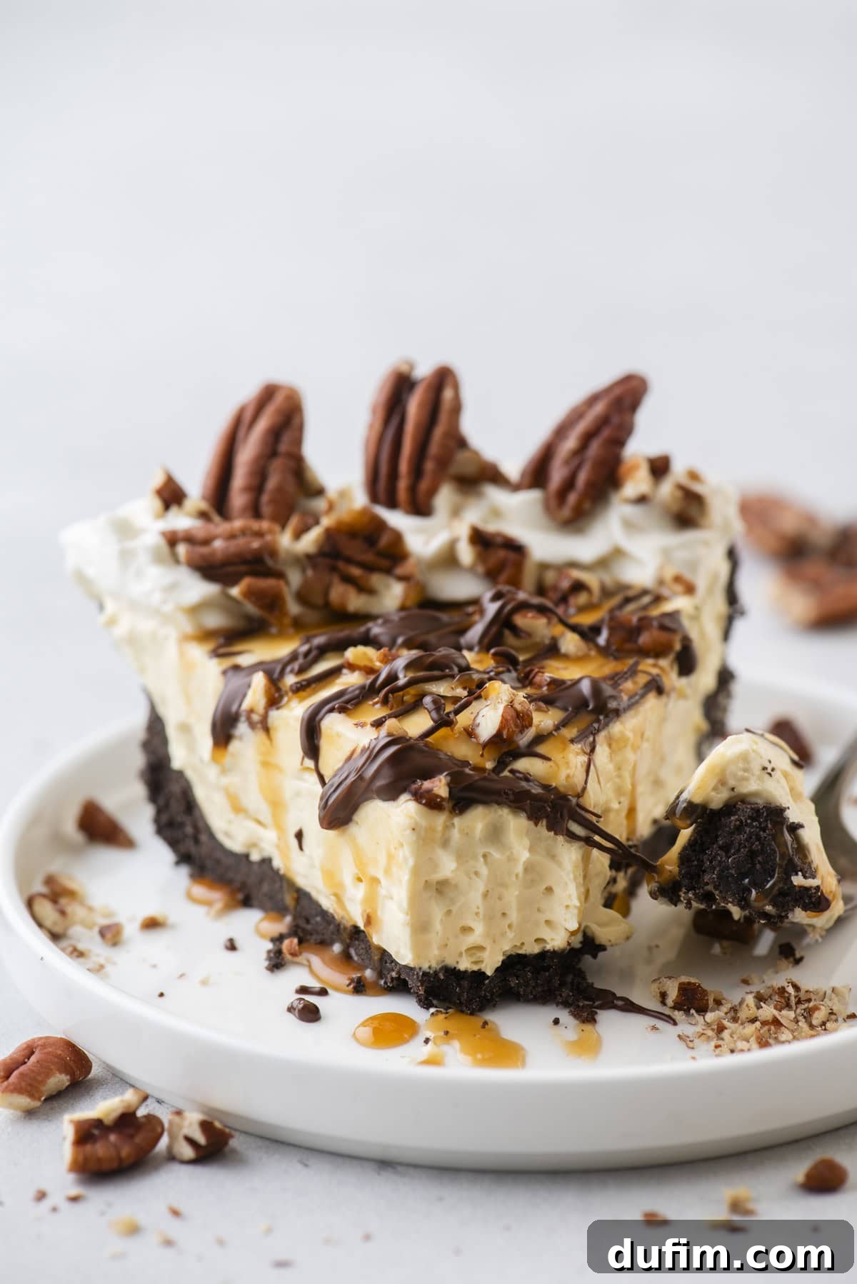 Caramel Pecan Chocolate Indulgence 3 A delectable slice of no-bake Turtle Pie presented on a small white plate, artfully garnished with chopped pecans, delicate chocolate drizzles, and golden caramel sauce, with extra pecan pieces scattered around for rustic charm.