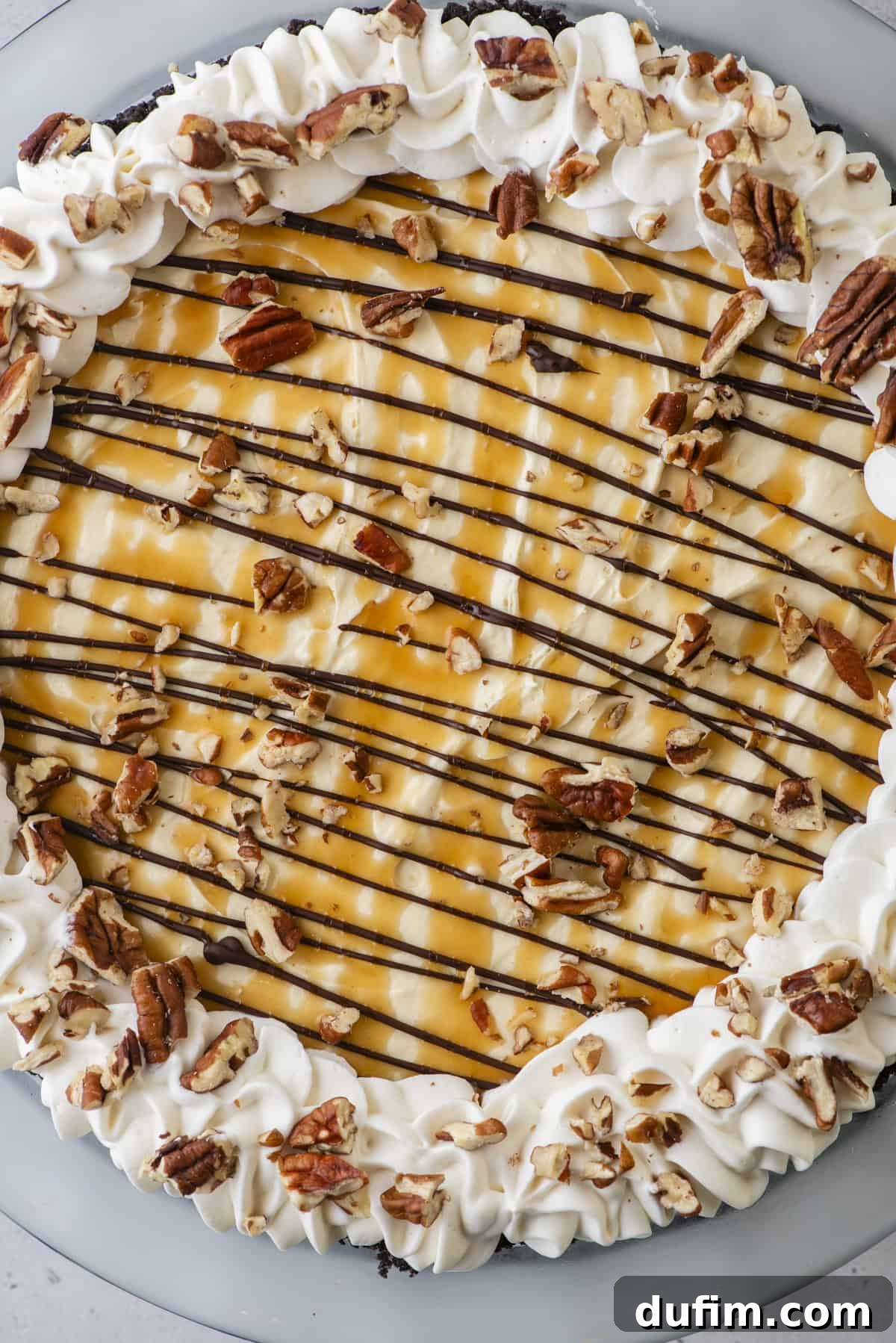 Caramel Pecan Chocolate Indulgence 4 An inviting overhead view of a complete no-bake Turtle Pie, beautifully adorned with generous dollops of whipped cream, intricate patterns of chocolate and caramel drizzles, and a generous sprinkle of pecans, creating an appealing visual spectacle.