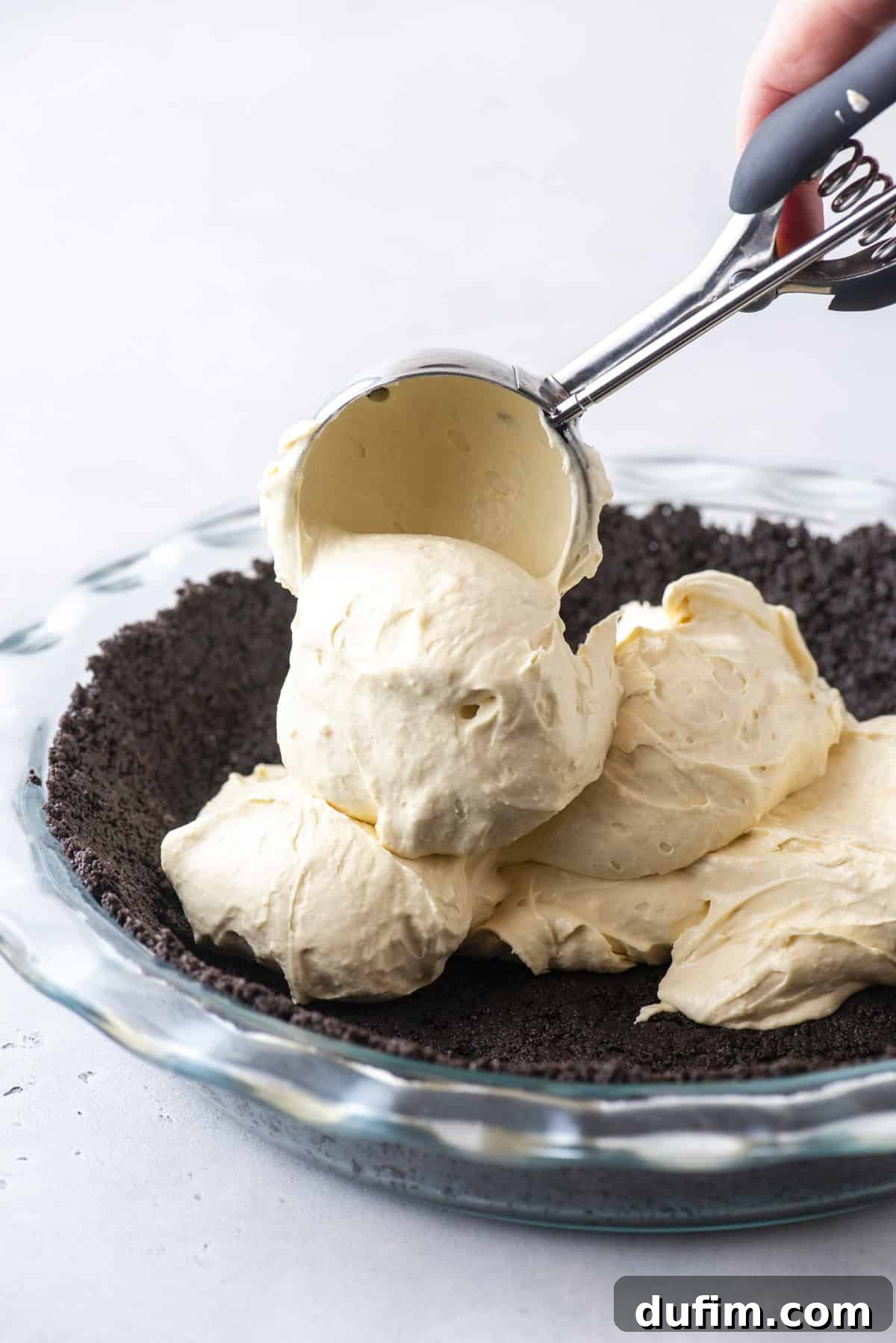 Caramel Pecan Chocolate Indulgence 6 Scooping the creamy caramel filling onto a freshly pressed Oreo crust in a clear glass pie dish, showing the luscious texture of the filling and the dark crust.
