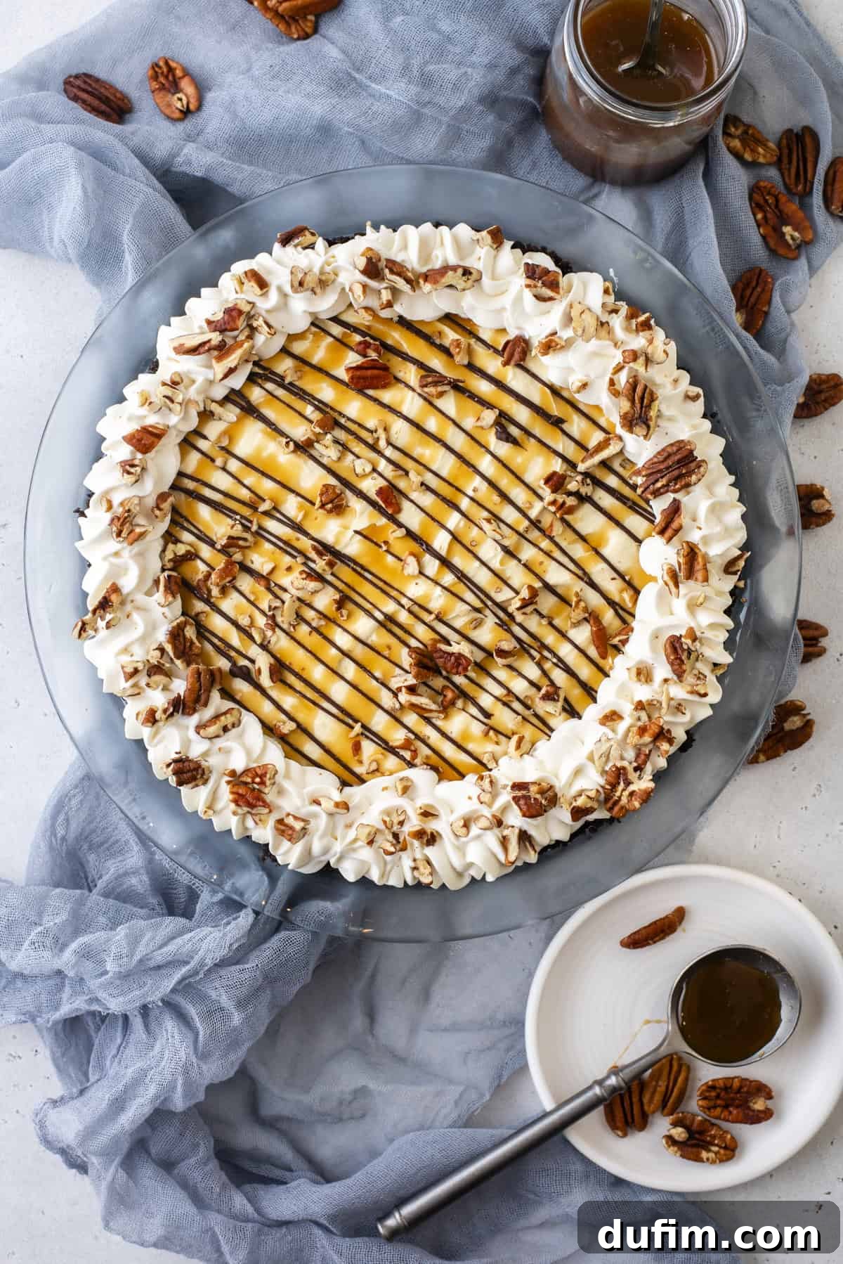 Caramel Pecan Chocolate Indulgence 8 An overhead shot of the fully adorned no-bake Turtle Pie, complete with a generous topping of caramel, chocolate, whipped cream, and scattered pecans, surrounded by additional pecan pieces and a bowl of caramel sauce.