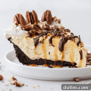 A slice of Turtle Pie topped with pecans, chocolate, and caramel drizzles on a small white plate.