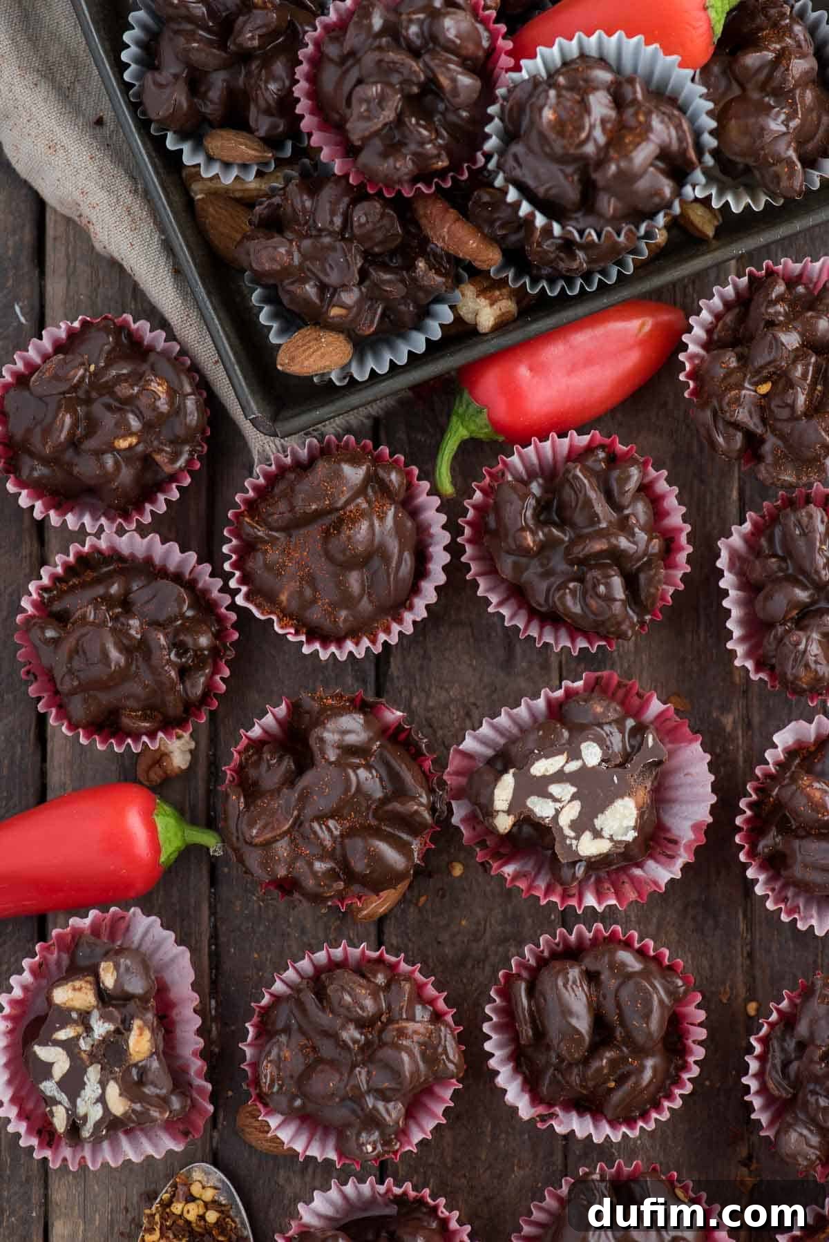 Crock pot or stove top spicy nut clusters! These dark chocolate cayenne nut clusters are popular during the holiday season. Plus there’s notes for making them less spicy or packed with heat! An inviting overhead shot of perfectly formed dark chocolate cayenne nut clusters in individual red mini muffin paper cups, showcasing their appealing texture and rich color.