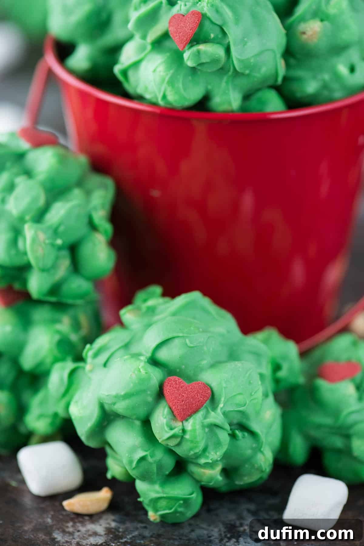 Close-up of several green Grinch candy clusters on a plate, featuring small red heart sprinkles and a light dusting of powdered sugar.