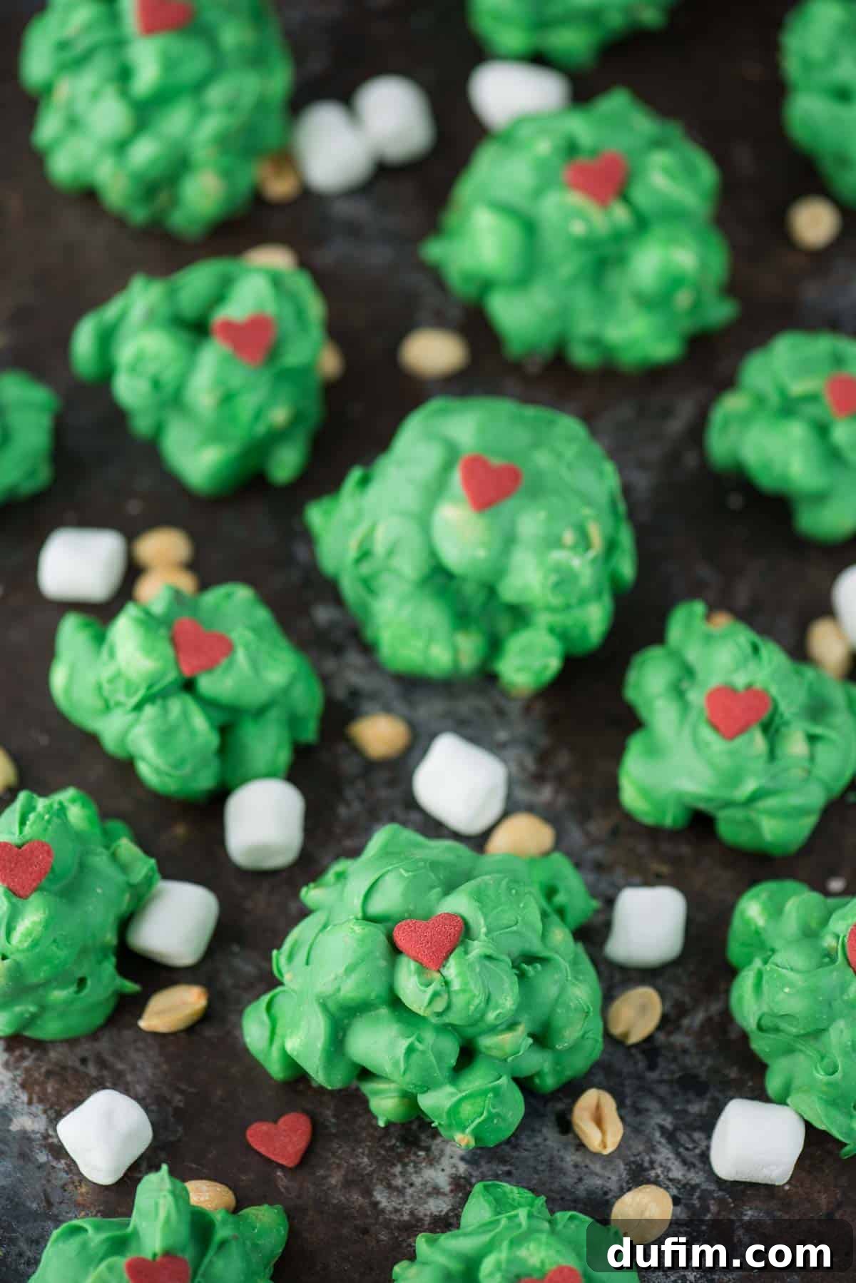 Green Grinch peanut marshmallow clusters with red heart sprinkles arranged on a white serving platter, ready for holiday festivities.