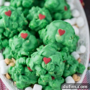 A plate of green, round Grinch candy treats decorated with red heart toppers, surrounded by mini marshmallows and peanuts, on a festive napkin.