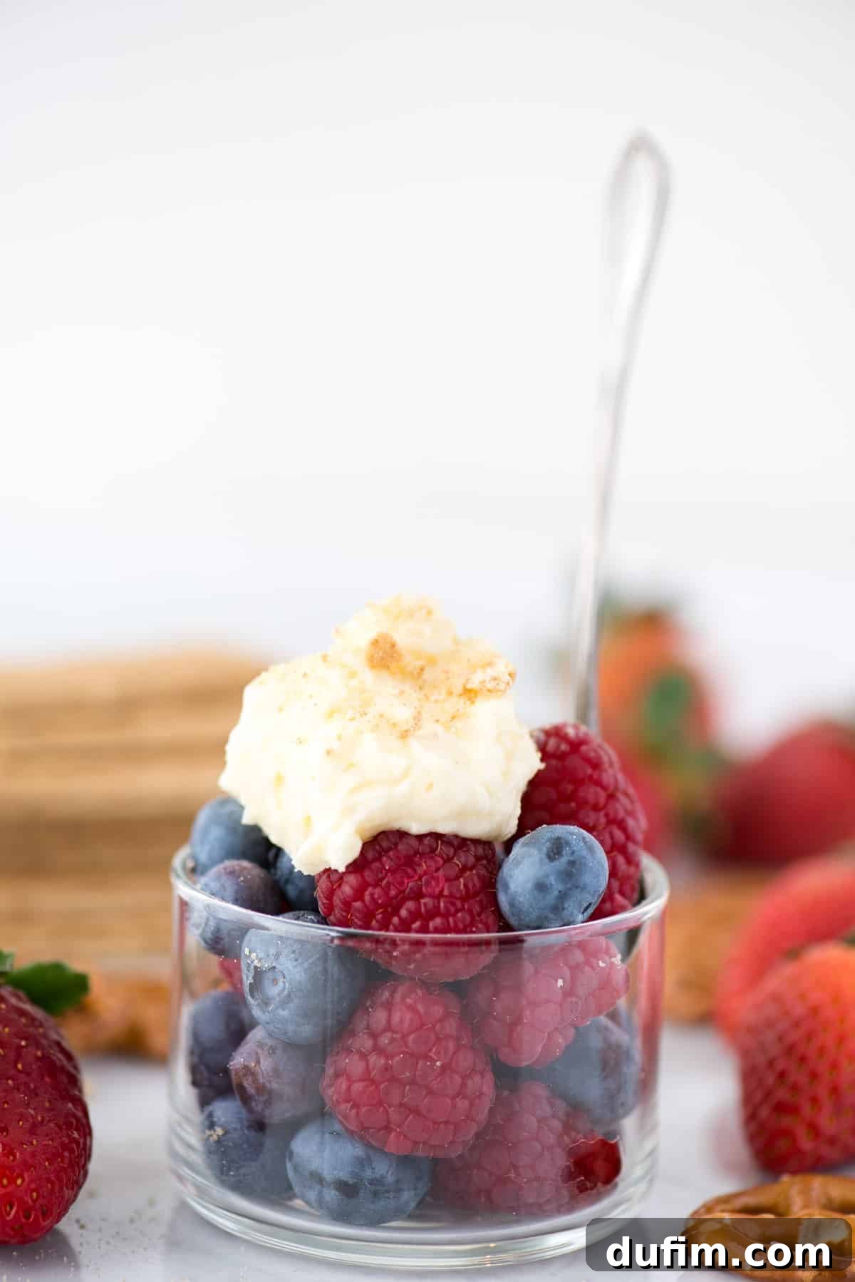 A bowl of fresh raspberries and blueberries generously topped with fluffy cheesecake flavored whipped cream, perfect for a refreshing dessert.