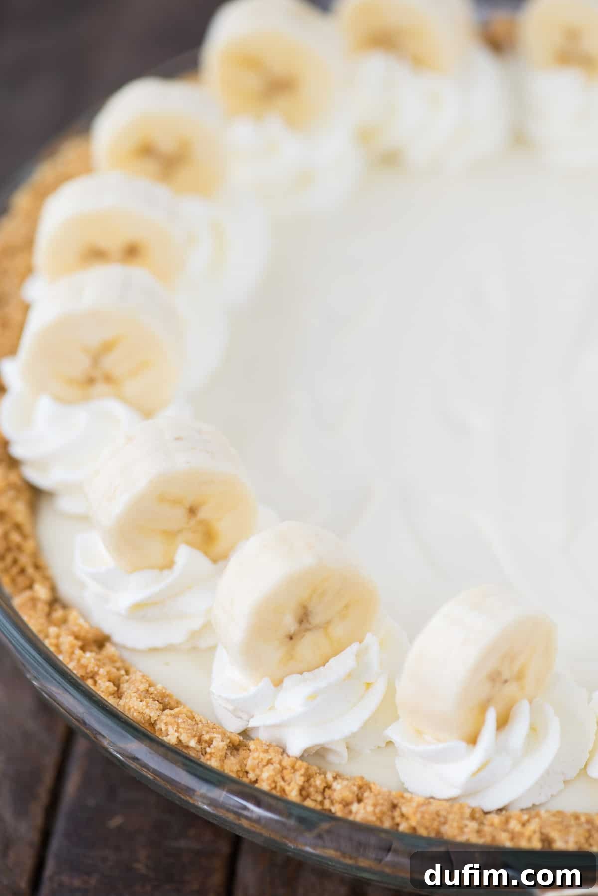 A delicious whole banana breeze pie, freshly assembled in a clear glass pie pan, ready to be chilled and enjoyed.