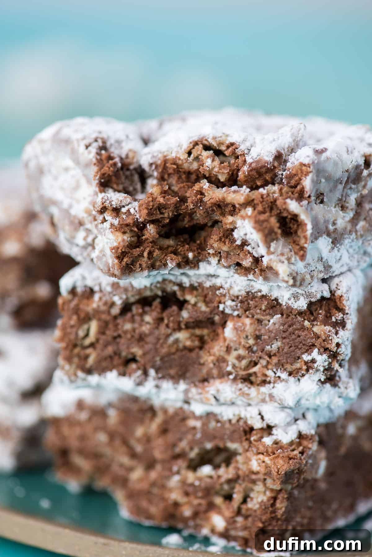 Three perfectly stacked Puppy Chow Bars on a teal background, dusted with powdered sugar.