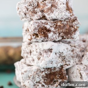 A stack of puppy chow bars dusted with powdered sugar sits on a plate, with a spoonful of peanut butter and scattered chocolate chips nearby.