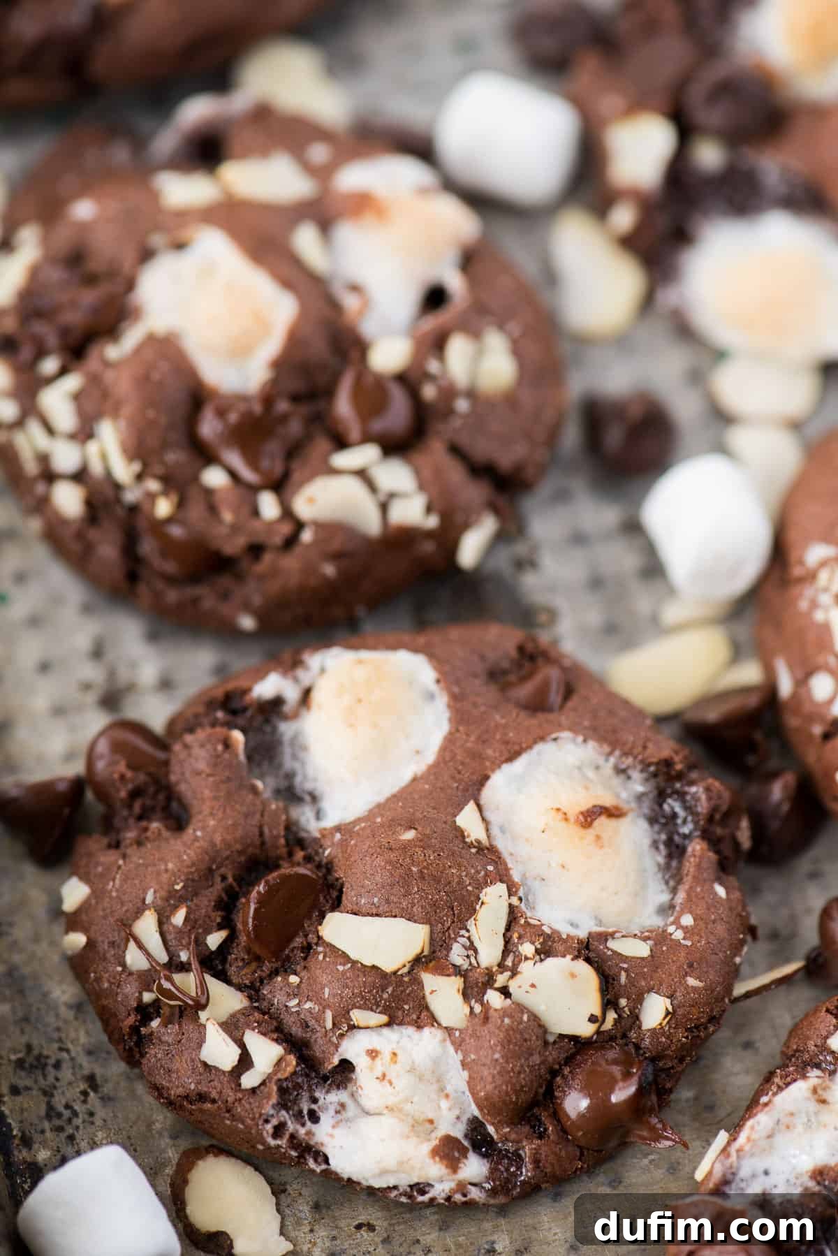 Soft and chewy rocky road cookies will hit the spot and remind you of your favorite rocky road ice cream. These chocolate cookies are packed with almonds, chocolate chips and marshmallows! You don’t have to chill the dough, this rocky road cookie recipe is ready in 30 minutes! Freshly baked rocky road cookies cooling on a metal baking sheet, featuring visible chocolate, almonds, and gooey marshmallow pockets.