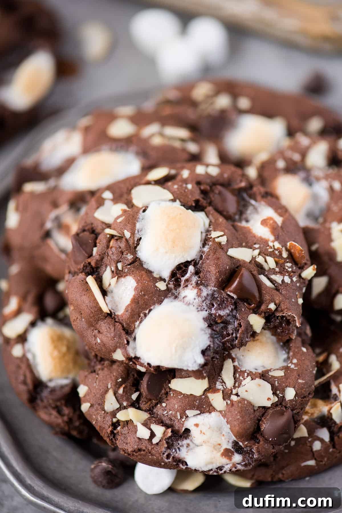 Soft and chewy rocky road cookies will hit the spot and remind you of your favorite rocky road ice cream. These chocolate cookies are packed with almonds, chocolate chips and marshmallows! You don’t have to chill the dough, this rocky road cookie recipe is ready in 30 minutes! A stack of warm rocky road cookies on a rustic metal plate, showing off their perfectly gooey texture and rich toppings.