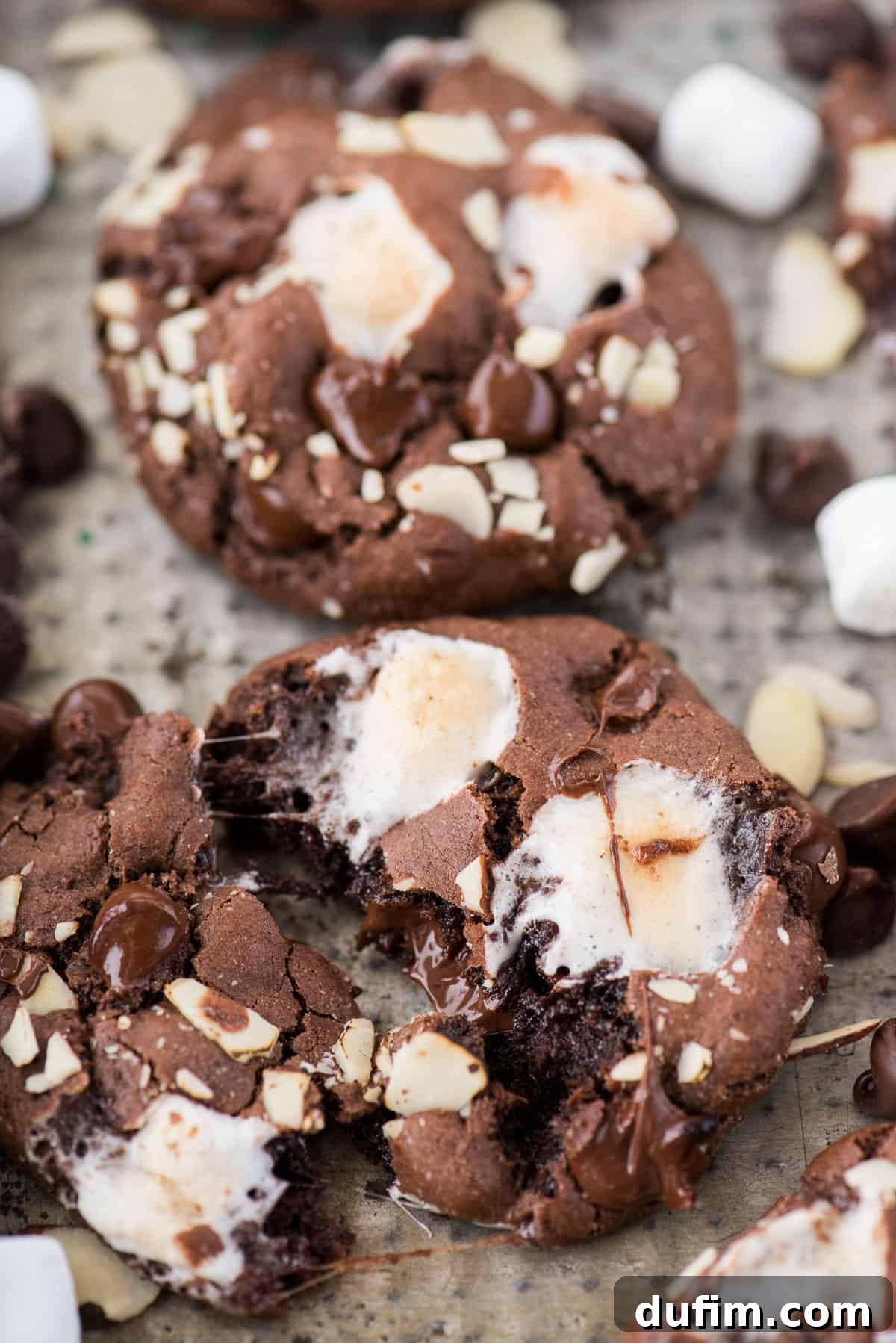 Soft and chewy rocky road cookies will hit the spot and remind you of your favorite rocky road ice cream. These chocolate cookies are packed with almonds, chocolate chips and marshmallows! You don’t have to chill the dough, this rocky road cookie recipe is ready in 30 minutes! A close-up of delicious rocky road cookies on a baking sheet, showcasing their warm, inviting texture with visible marshmallows and chocolate.